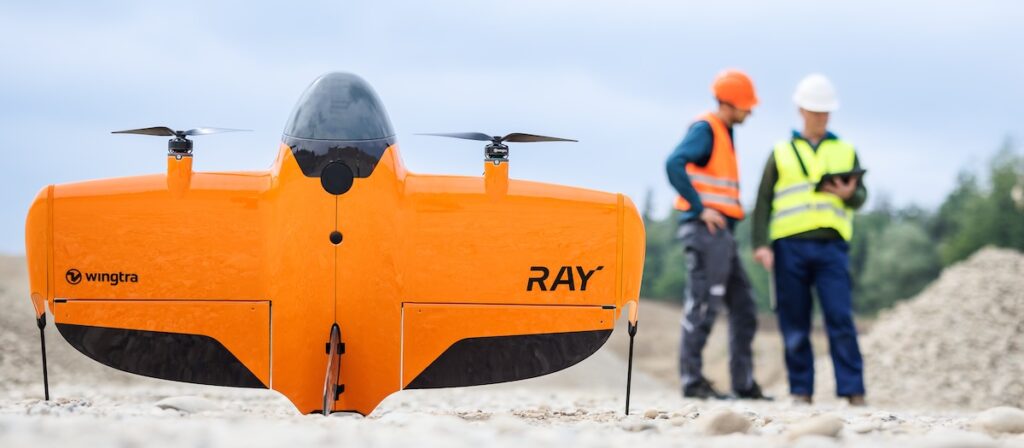 Fixed-wing VTOL drone WingtraRAY standing on the floor next to two surveyors
